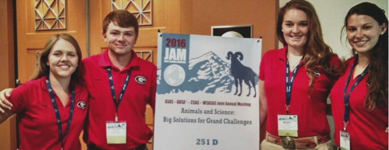 Four UGA dairy quiz bowl team members posing with a convention banner the middle.