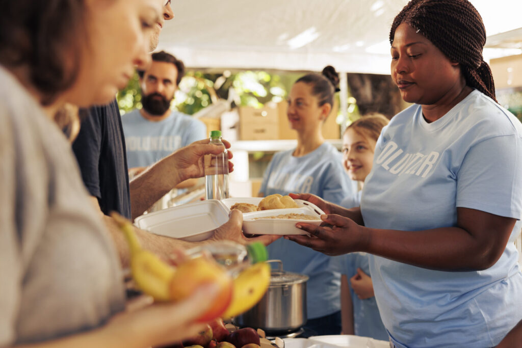 Image of outdoor food drive with middle aged Black woman wearing a light blue tshirt serving a plate of food.