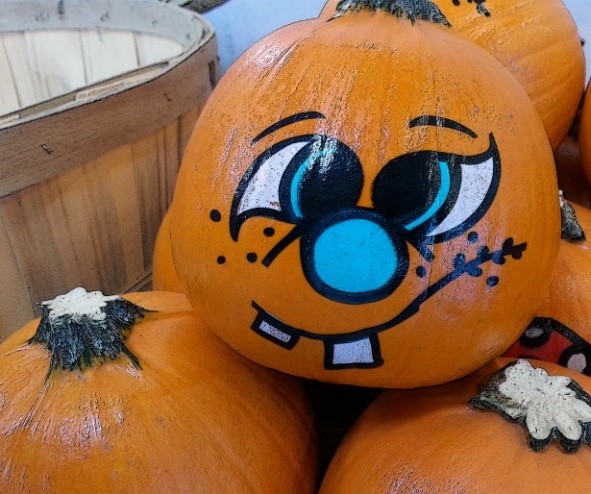 A box of pumpkins, the top one painted with a silly face.