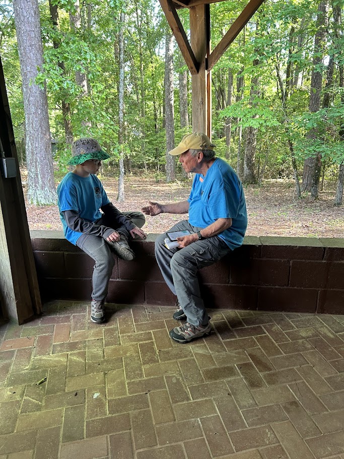 An adult male and an elementary student sit under a pavilion