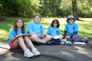 4 youths from 4th-6th grade sitting outdoors in matching blue t-shirts