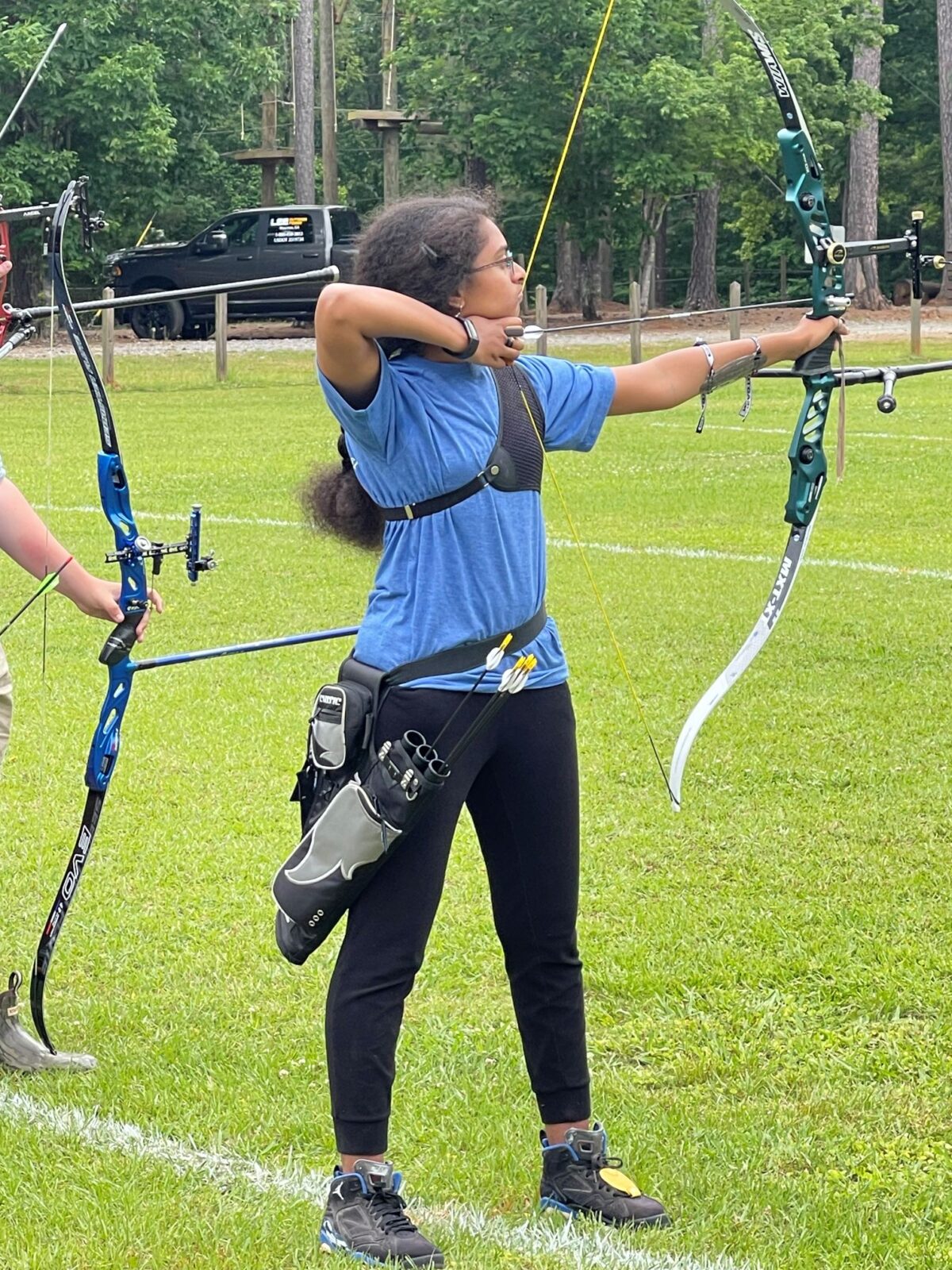 A high school female archery with her recurve bow drawn back, ready to shoot