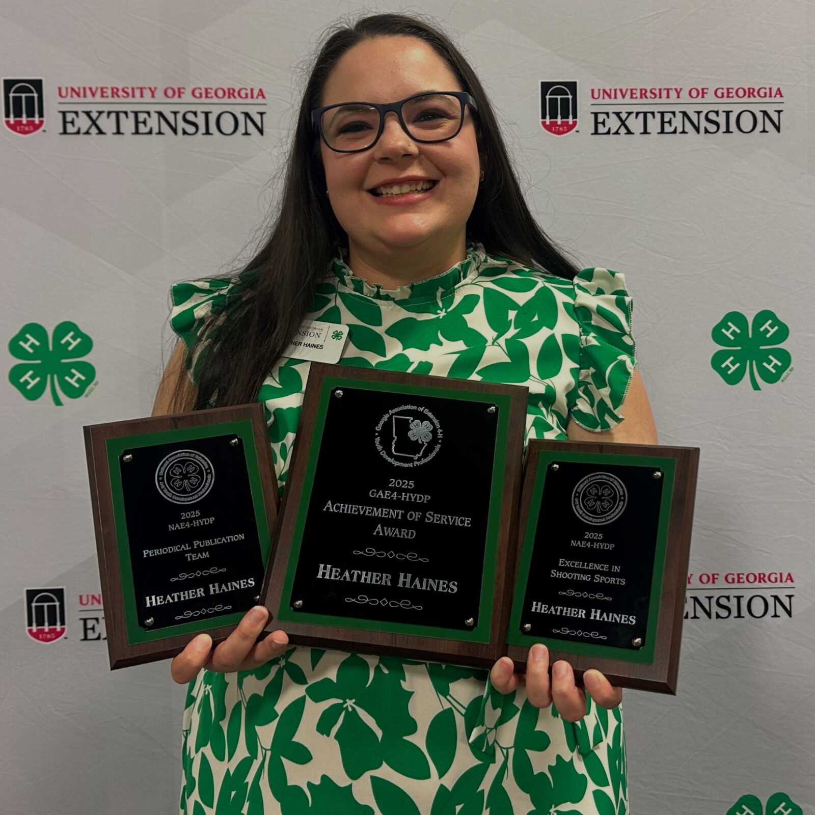 An adult woman holding three plaques representing professional accomplishments