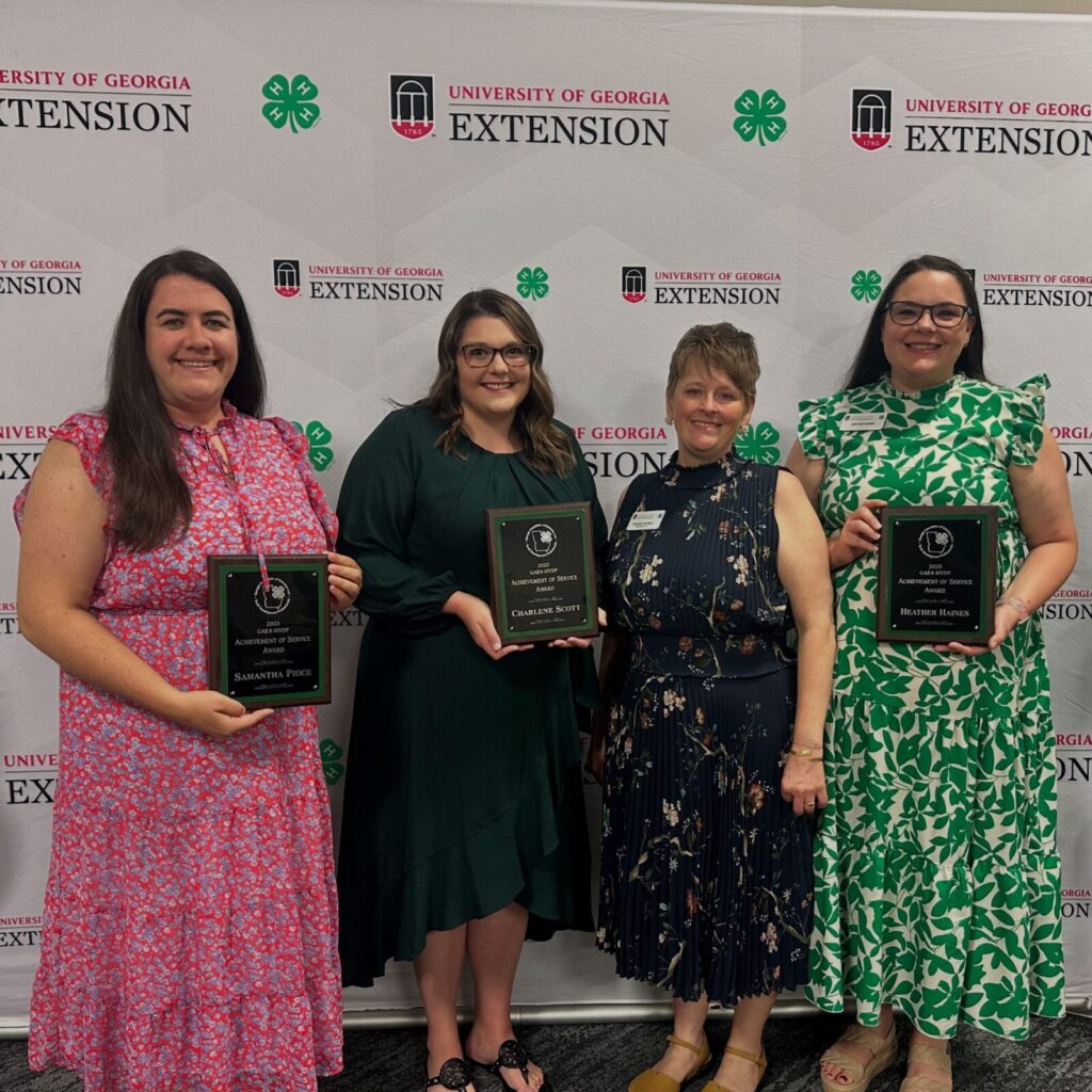 Four women, three holding plaque awards, pose for a photo