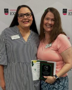 Two adult women, one holding an award, pose for a photo