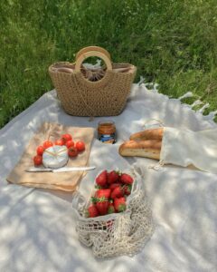 White picnic blanket with bread, cheese, tomatoes, and strawberries.