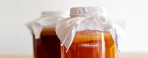 Two glass jars with amber colored liquid. They have a white cloth on top, tied with a white string.