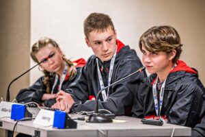 Three middle school students sitting at a table with microphones.