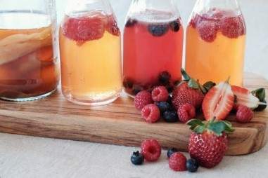 4 clear jars filled with amber colored liquid and various types of fruit.