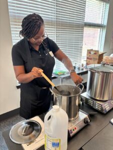 A female college student working over a hot plate which has a large pot of boiling water resting on top.
