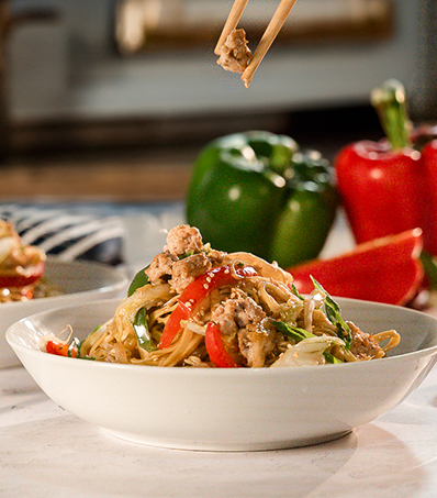 Pork Chow Mein in a white bowl with bell peppers in the background