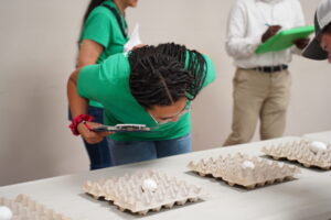 A middle school girl holding a clipboard leaning over an egg to examine it