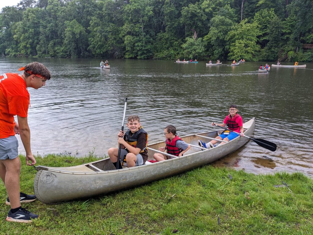 Students in a canoe being assisted by a camp counselor.
