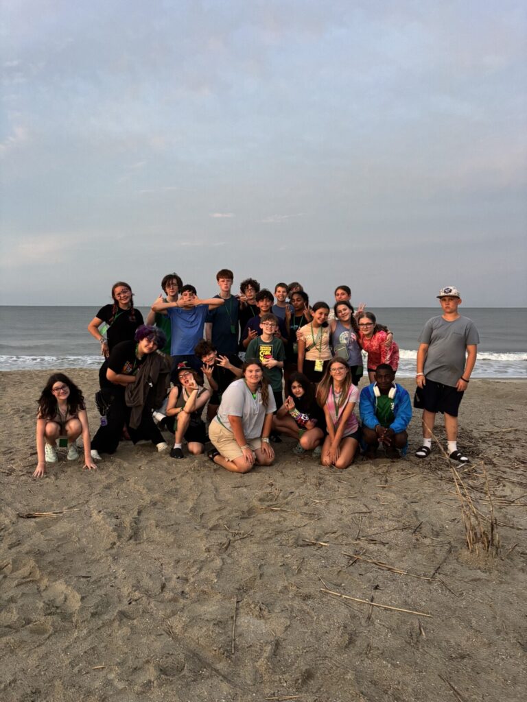 A group of students standing on the beach in front of the ocean. 