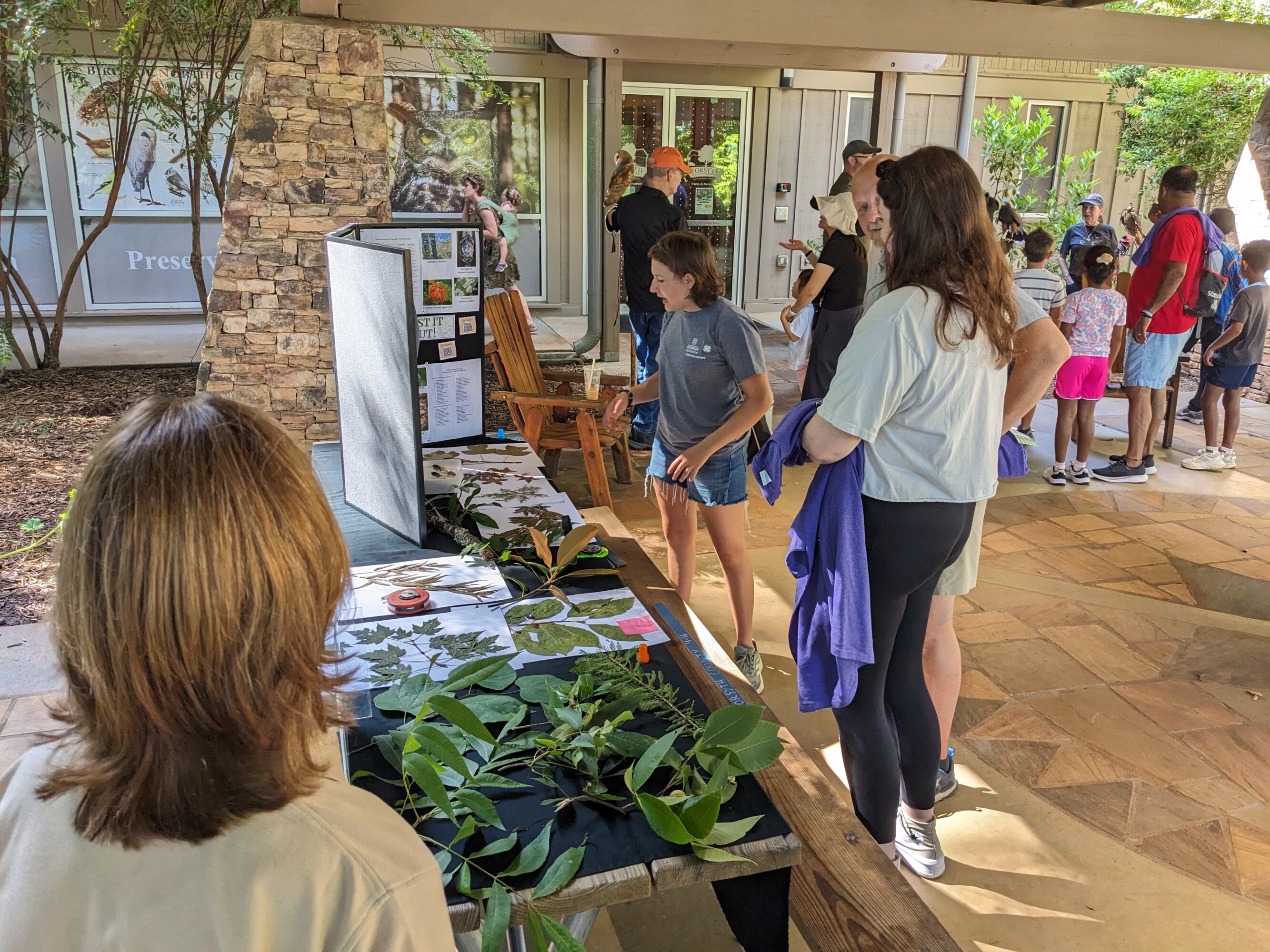 Guests at a wildlife event standing at a booth as a teen teacher talks to them about forestry