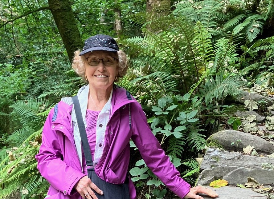 the author in a purple jacket leaning against a rocky ledge in the woods