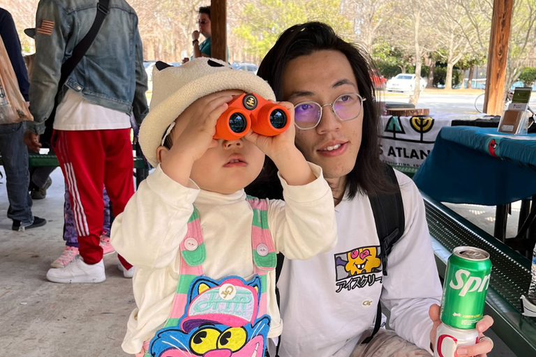 A child with binoculars and a person holding a Sprite can at an outdoor gathering.