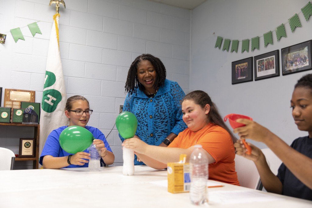 An adult leader mentoring three youth during a science activity with balloons.