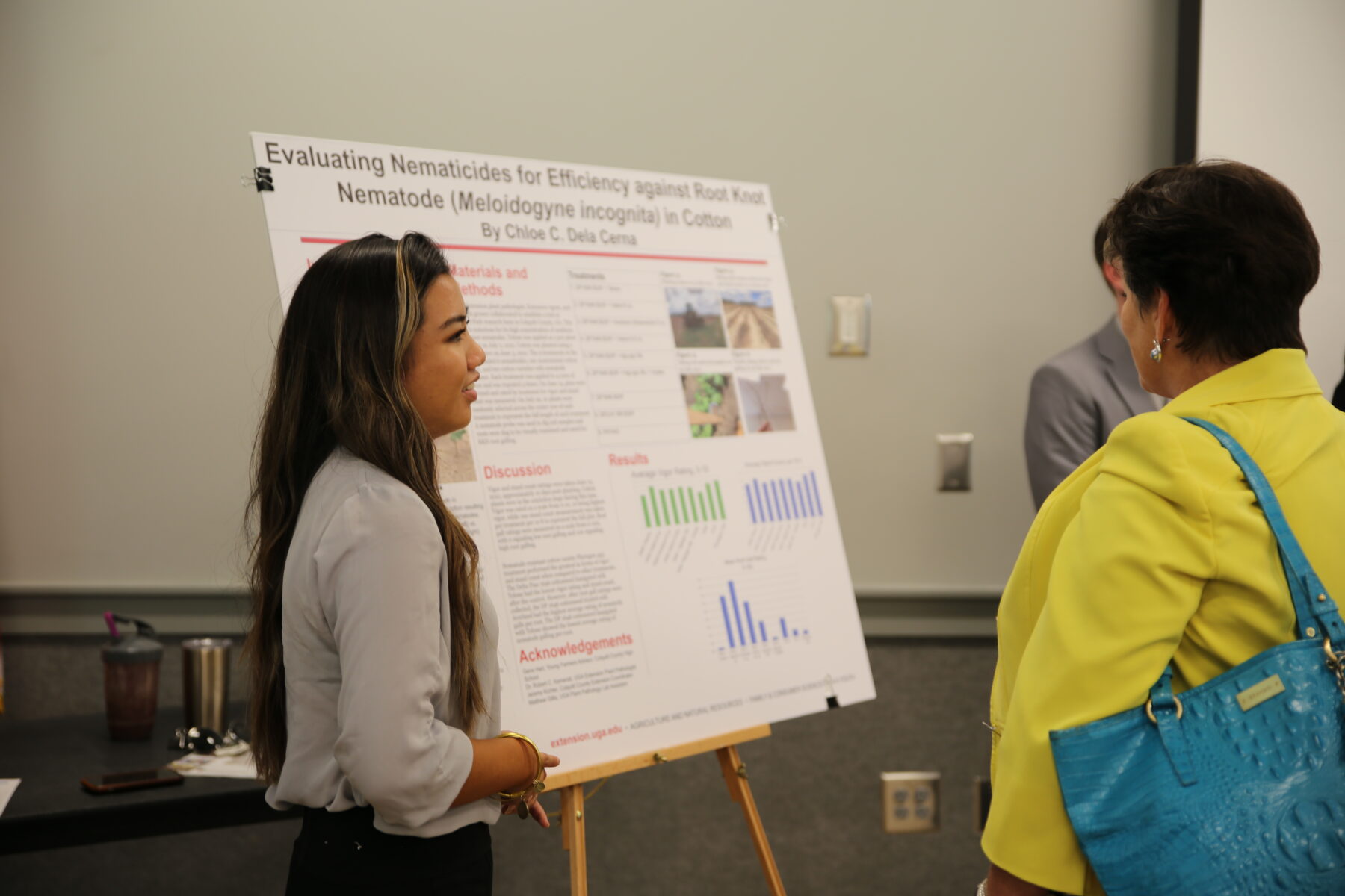 A woman presents a research poster while another person listens attentively.