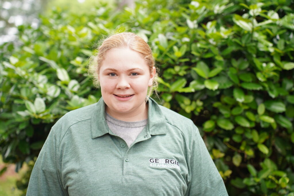 teenage girl wearing a green Georgia 4-H Ambassador polo standing next to a tree