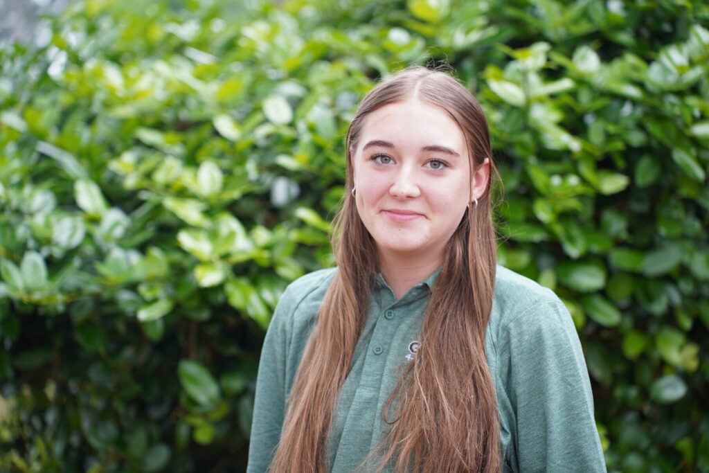 teenage girl wearing a green Georgia 4-H Ambassador polo standing next to a tree