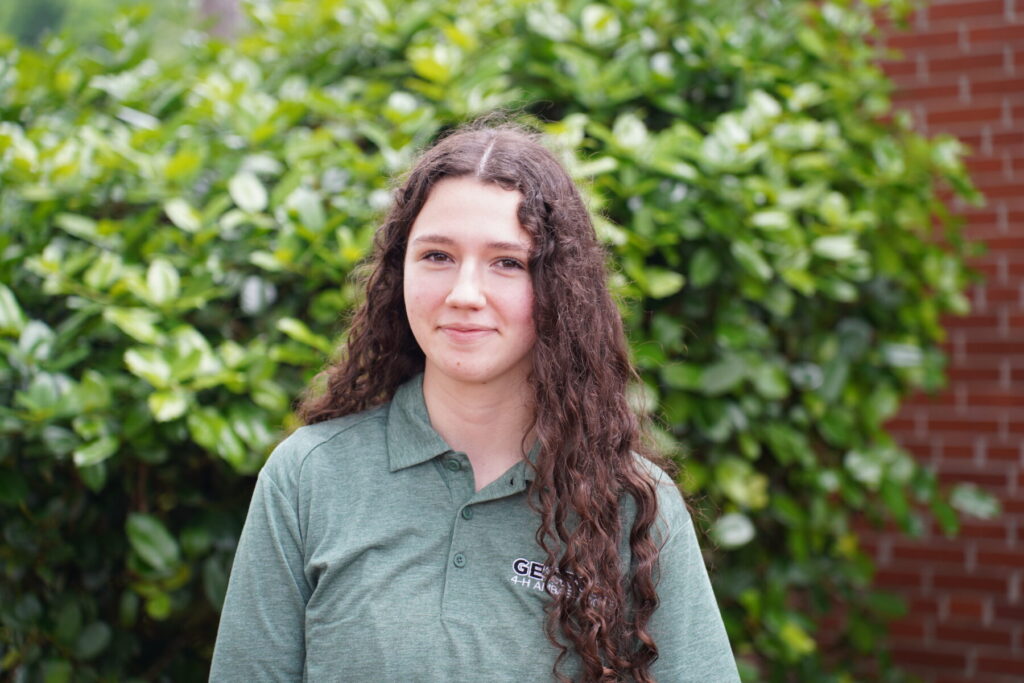 teenage girl wearing a green Georgia 4-H Ambassador polo standing next to a tree