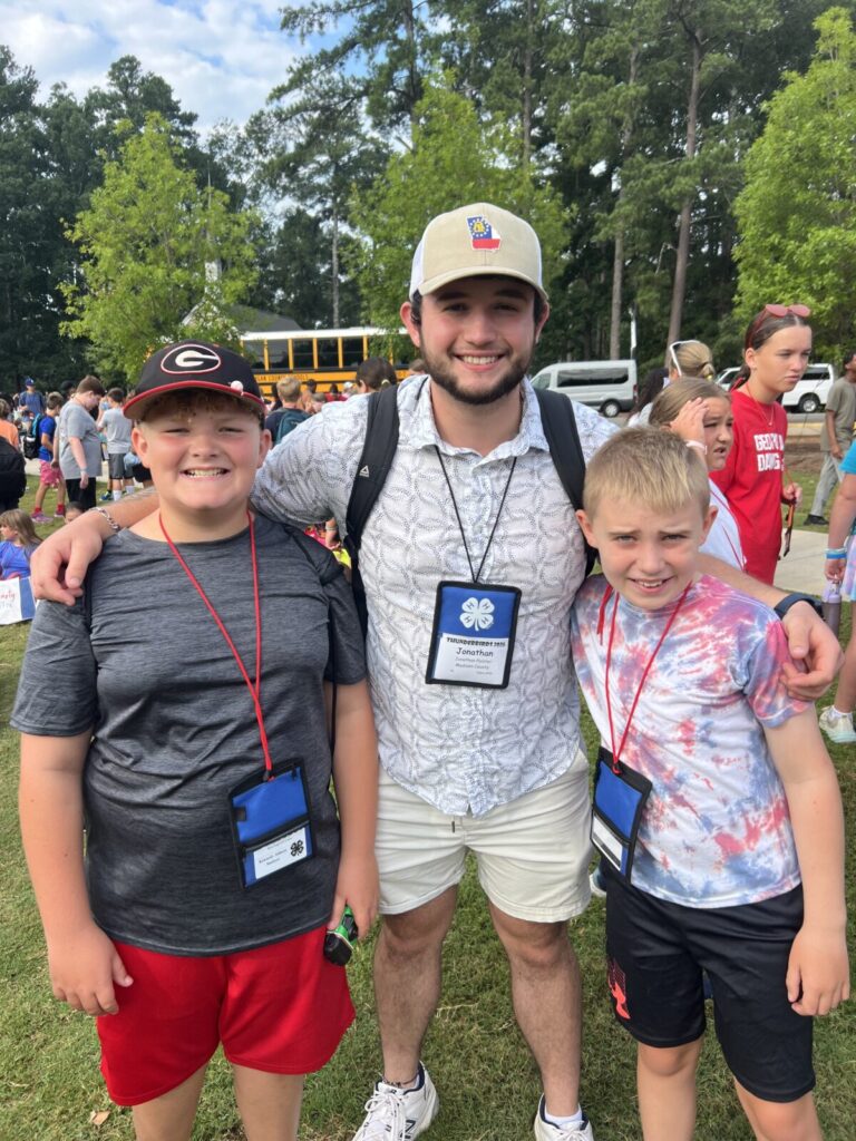 two young boys smiling and standing on either side of a male adult volunteer