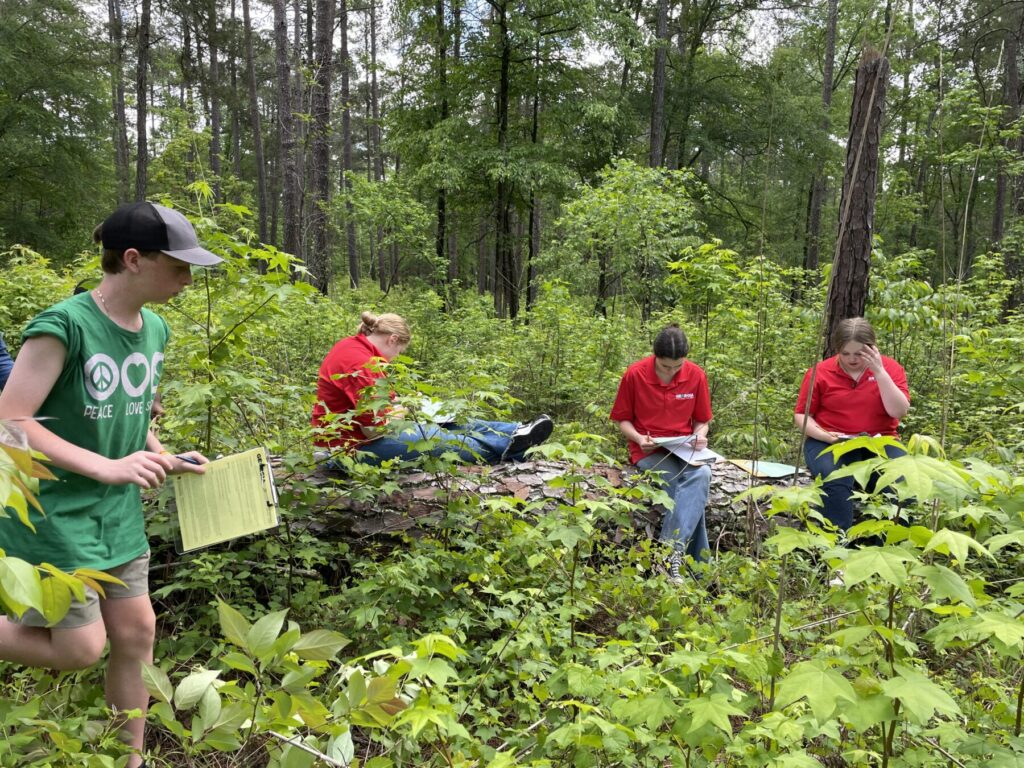 two teenage girls wearing red shirts in sitting on a log in the woods