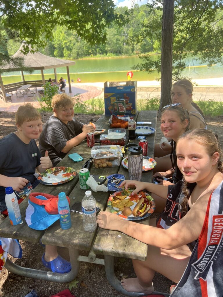 Five teens at a picnic table eating hotdogs