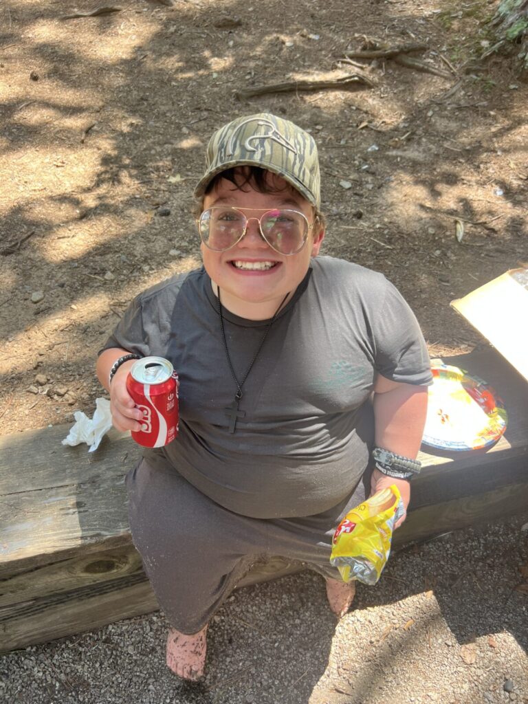 Male teen sitting on a piece of wood holding a soda and chips