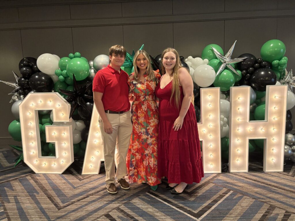 female adult leader standing between a teen male and teen female all wearing red clothes