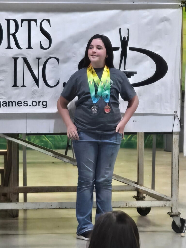 Teenage girls standing with hands on hips wearing medals around her neck.