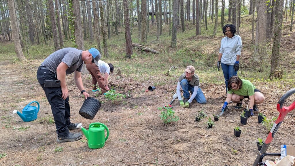 Five gardeners planting shade tolerant, pollinator garden/  Plants on the ground and installation in progress.